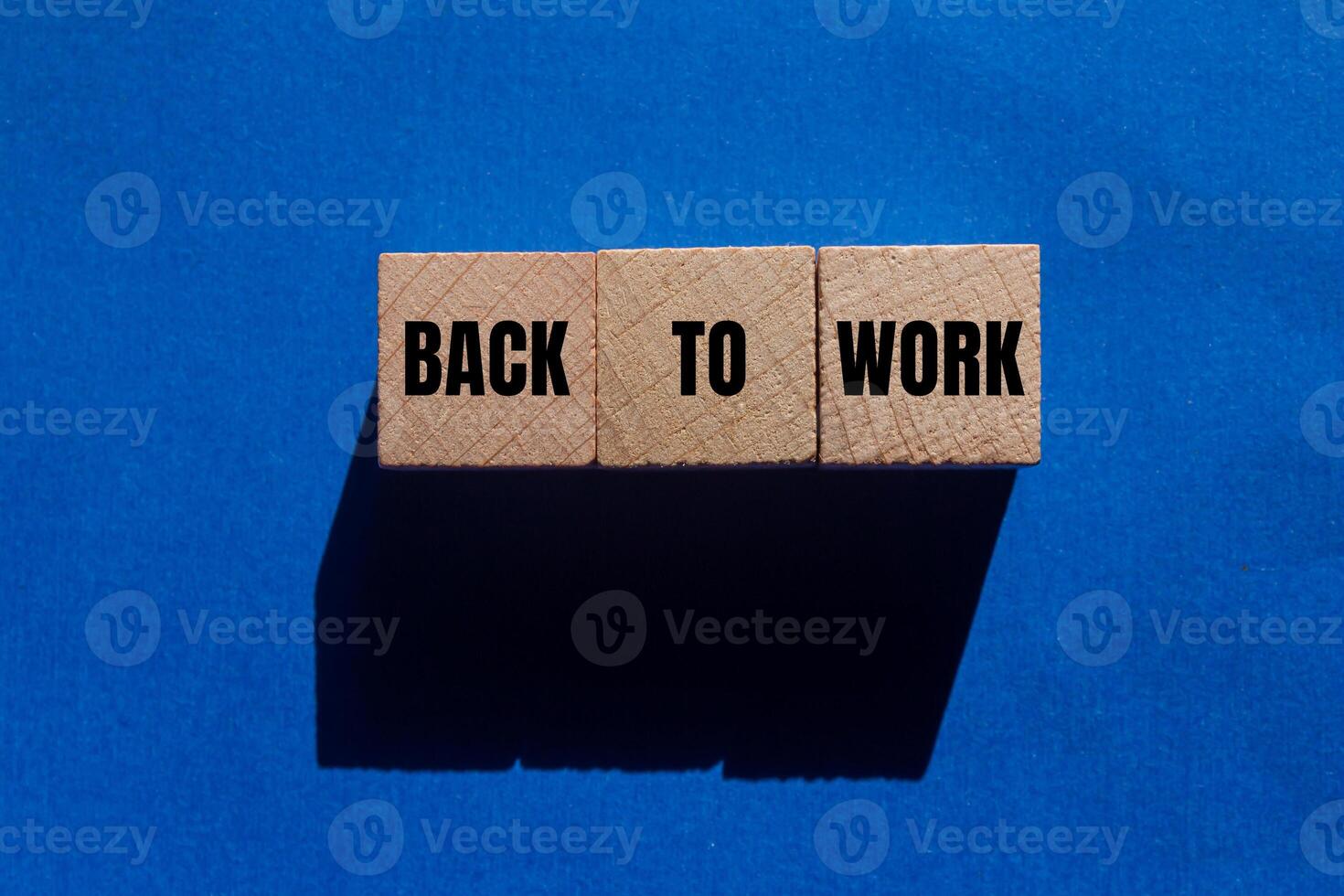 Back to work message written on wooden cubes on blue background. Conceptual back to work symbol. Copy space photo