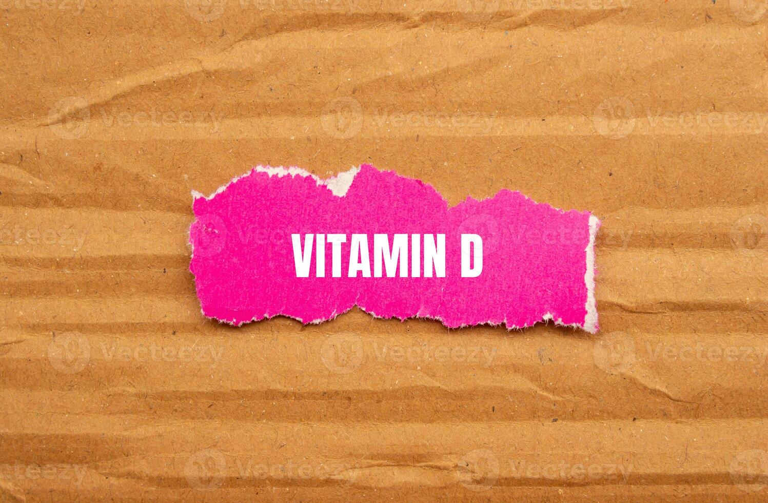 Vitamin d message written on ripped pink torn paper piece with cardboard background. Conceptual vitamin d symbol. Copy space. photo