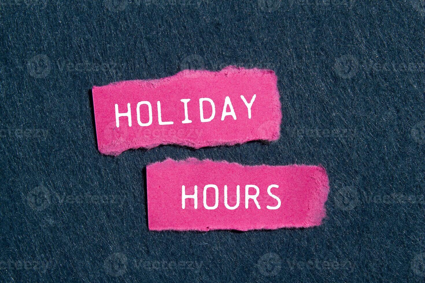 Holiday hours message written on ripped pink torn paper pieces with gray felt background. Conceptual holiday hours symbol. Copy space. photo