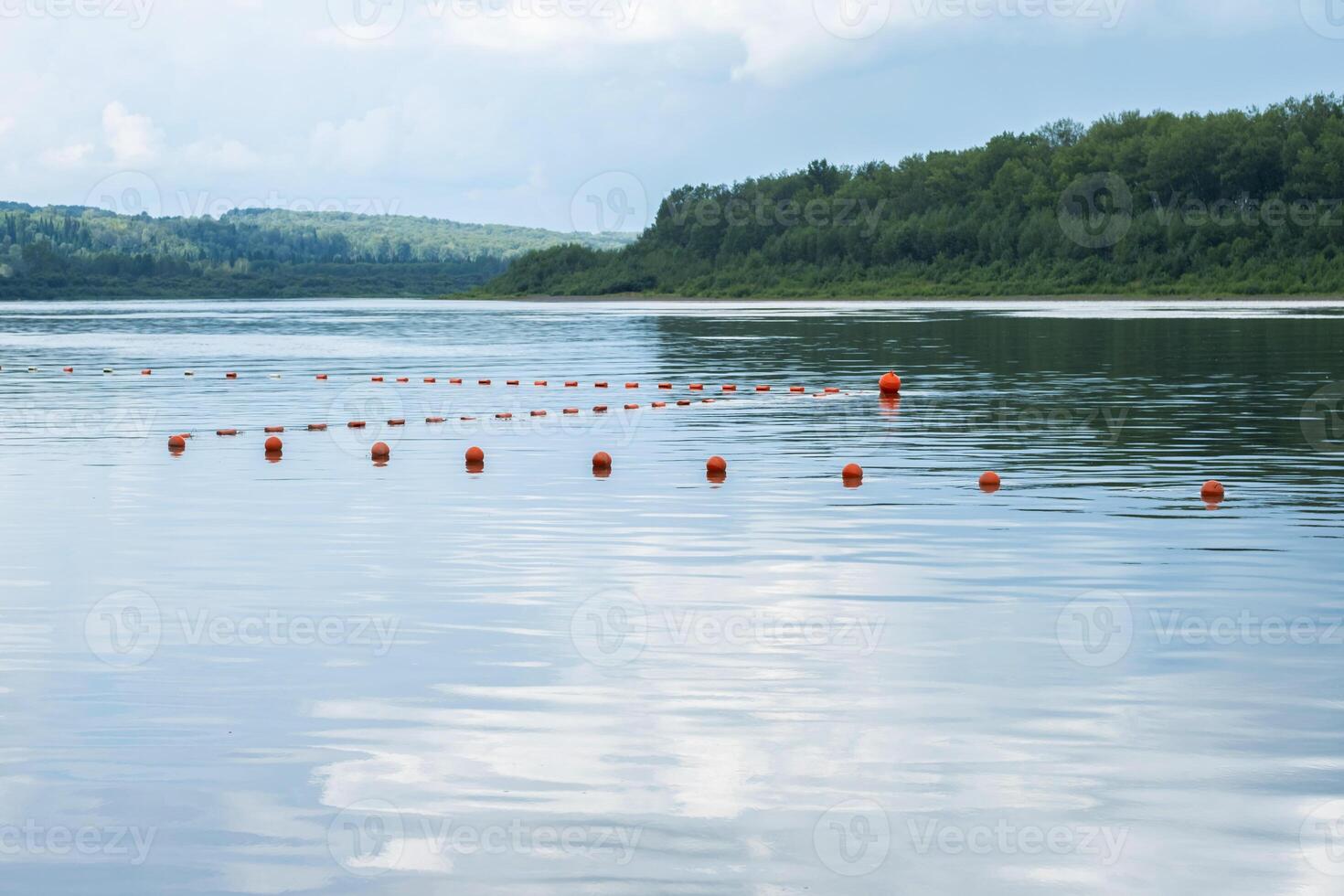 Orange buoys floating on a calm lake with forested shore in the background. photo