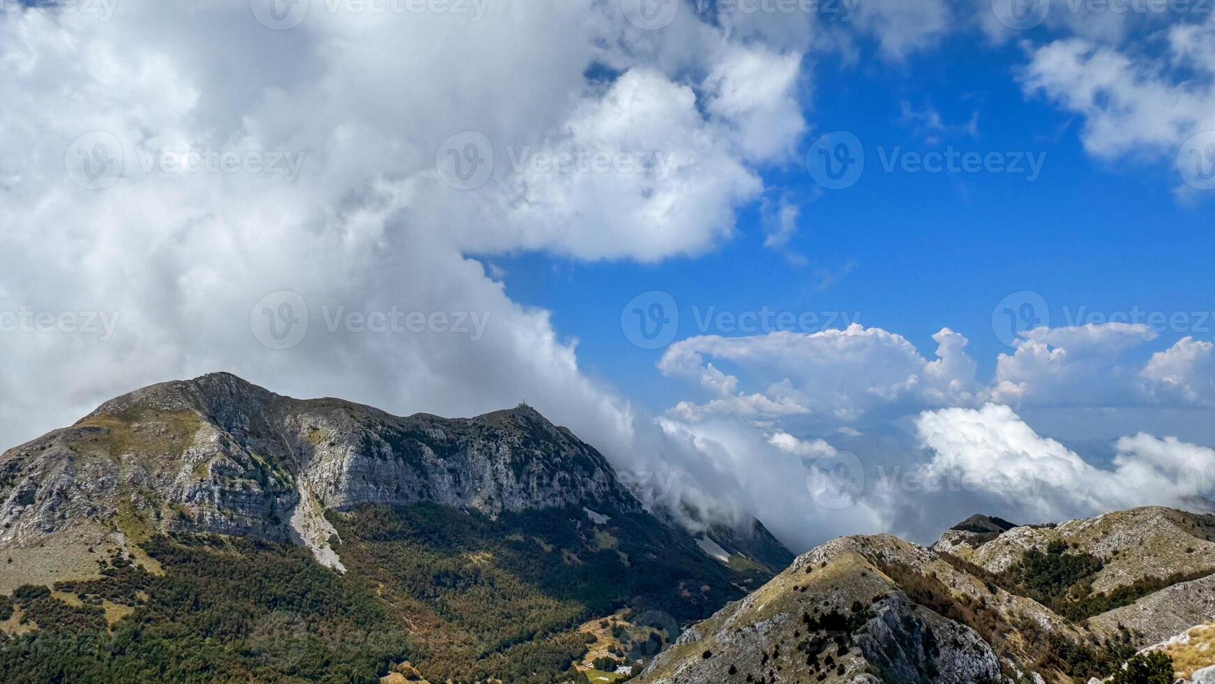 A scenic view of a mountain range with lush greenery and cloud-covered peaks, under a bright blue sky. photo