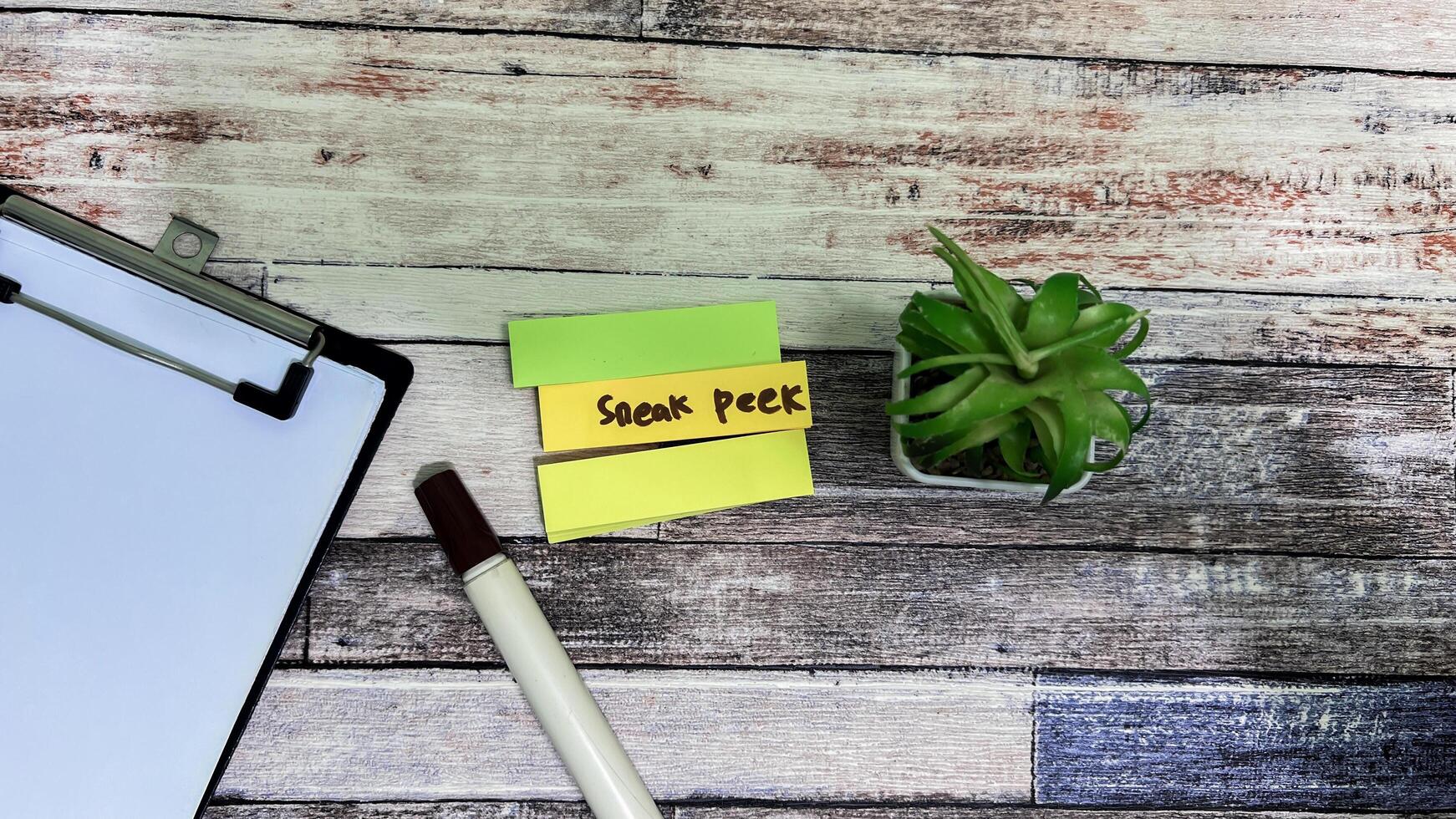 Concept of Sneak Peek write on sticky notes isolated on Wooden Table. photo