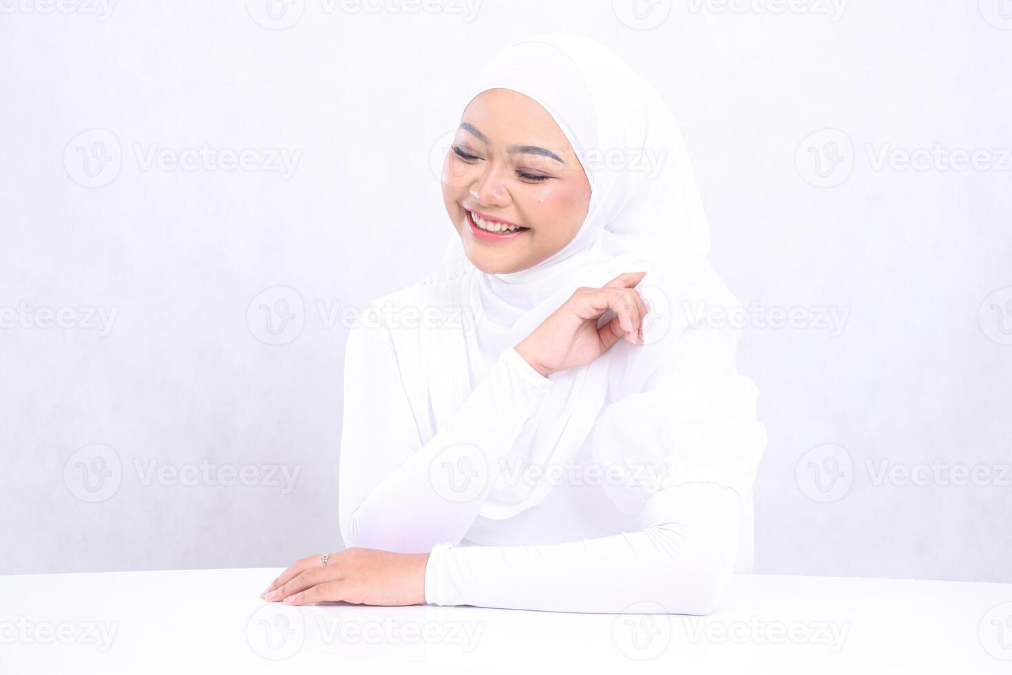 charm of veiled girl asian laughing down with perfect and healthy radiant white skin, hands on table and left arm isolated white background. closeup of face makeup for skincare, health, care content photo