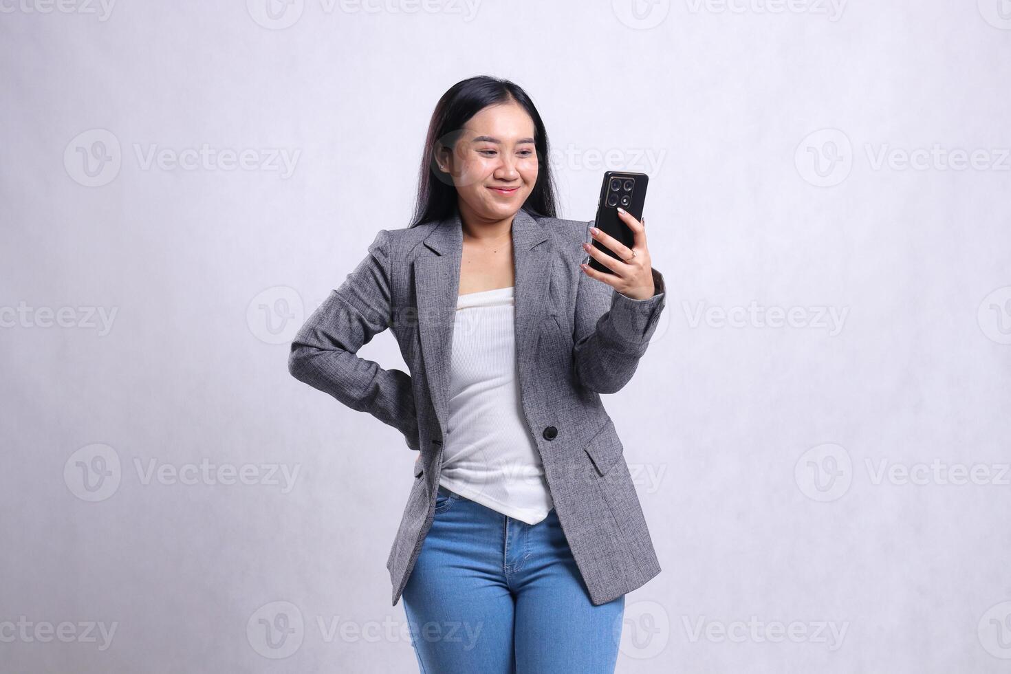 beautiful young office woman smile to mobile phone hold waist, holding cellphone wearing gray suit isolated on white background. for technology, lifestyle, shopping, transaction content photo