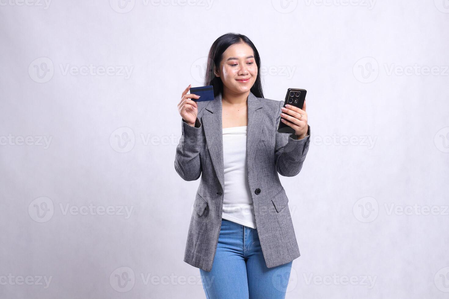 beautiful young woman office smile hold mobile phone smartphone and hold credit debit member card wearing grey suit isolated on white background. for communication, finance, transaction content photo