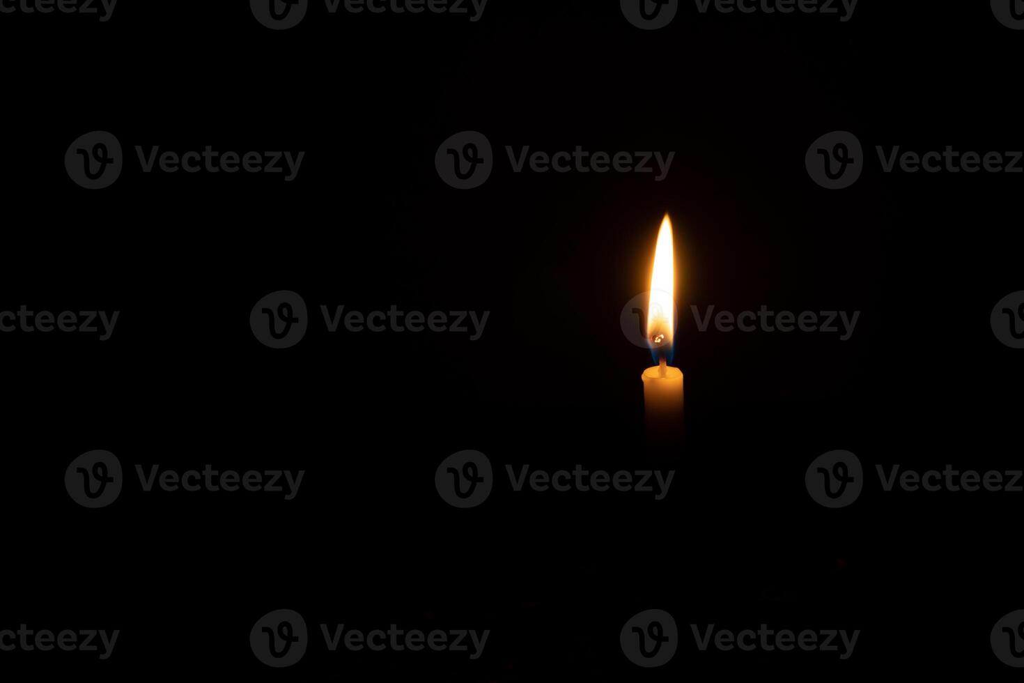 A single burning candle flame or light glowing on a small orange candle on black or dark background on table in church for Christmas, funeral or memorial service with copy space photo