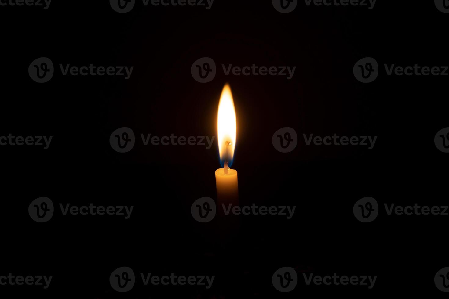 A single burning candle flame or light glowing on a small orange candle on black or dark background on table in church for Christmas, funeral or memorial service with copy space photo