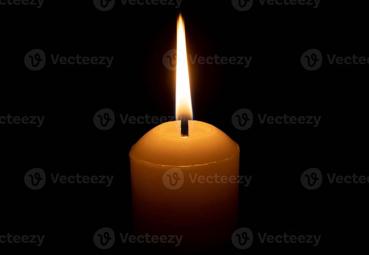 A single burning candle flame or light glowing on a big white candle isolated on red or dark background on table in church for Christmas, funeral or memorial service photo