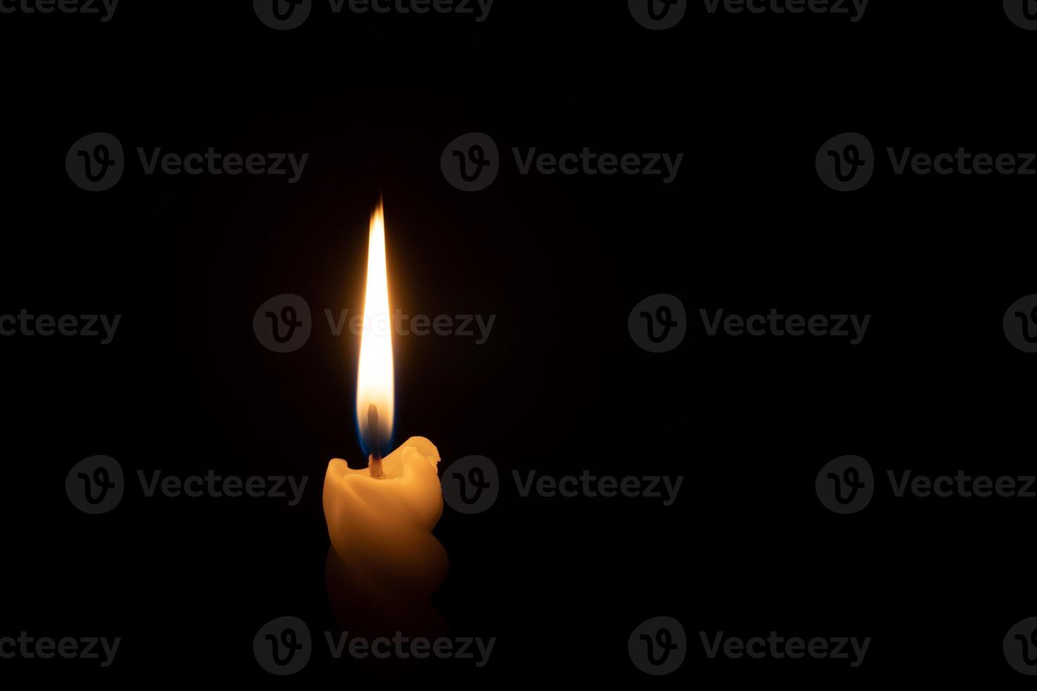 A single burning candle flame or light glowing on a spiral white candle on black or dark background on table in church for Christmas, funeral or memorial service with copy space photo