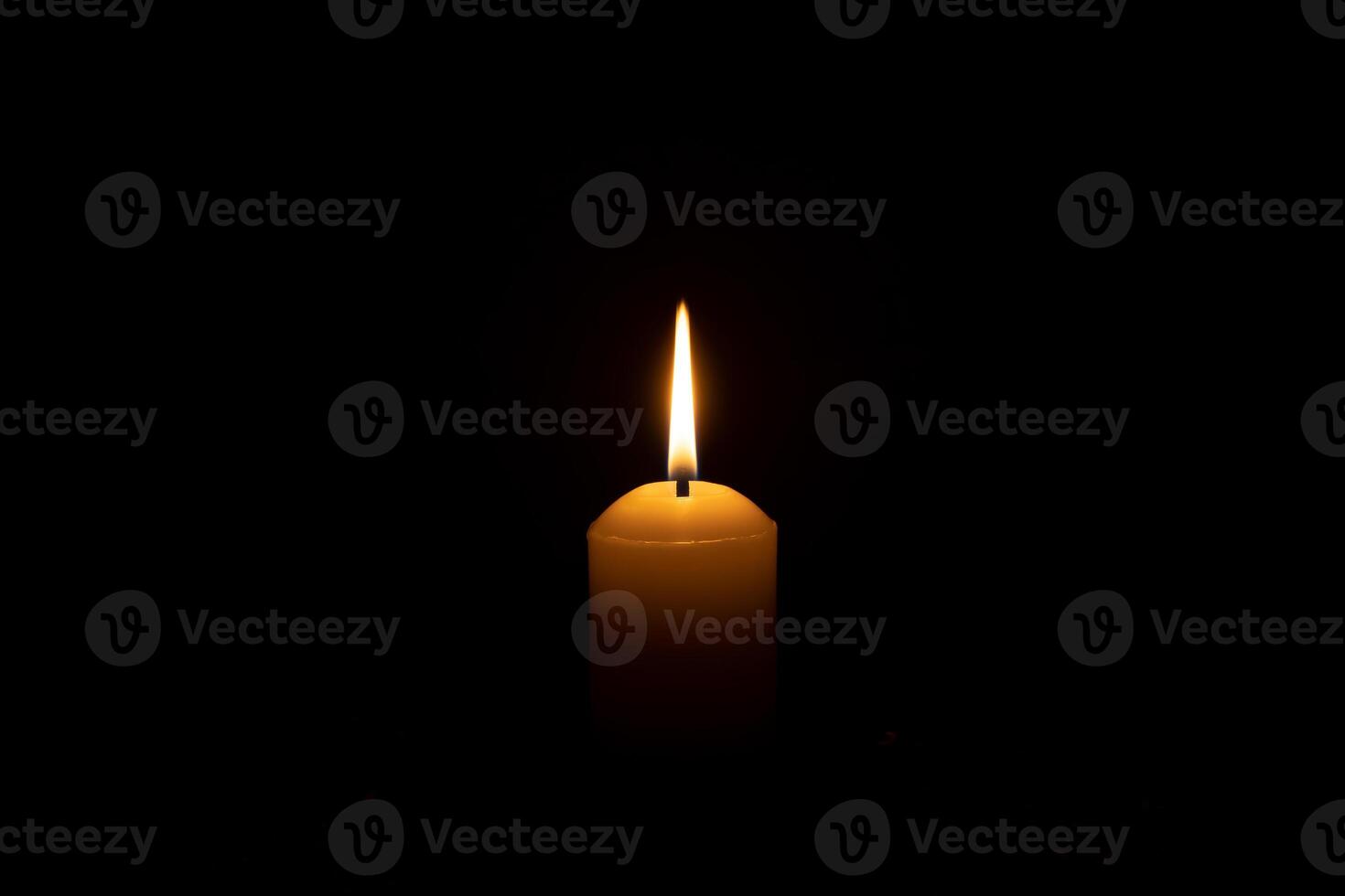 A single candle light glowing on a big white candle on table in church for Christmas, funeral or memorial service with copy space isolated on black background photo