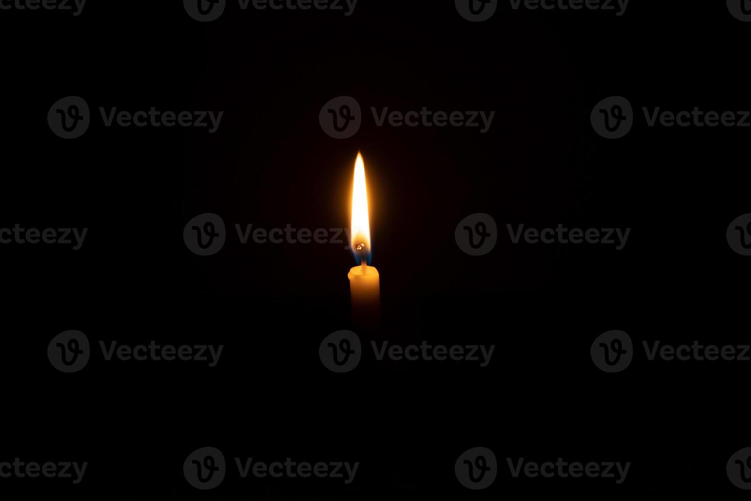 A single burning candle flame or light glowing on a white candle on black or dark background on table in church for Christmas, funeral or memorial service with copy space photo