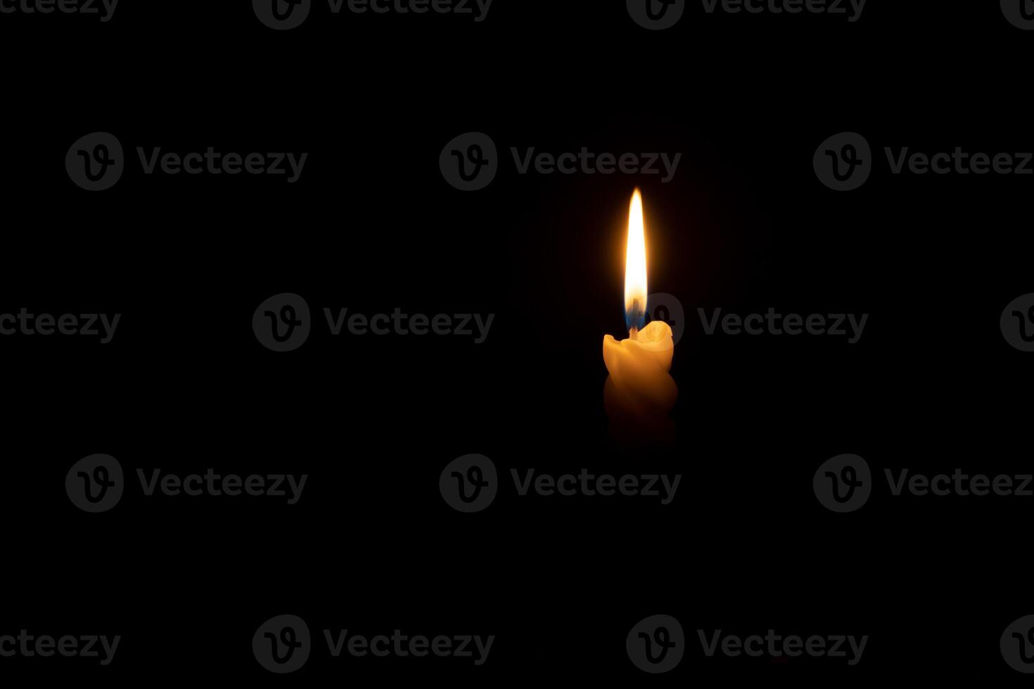 A single burning candle flame or light glowing on a spiral white candle on black or dark background on table in church for Christmas, funeral or memorial service with copy space photo