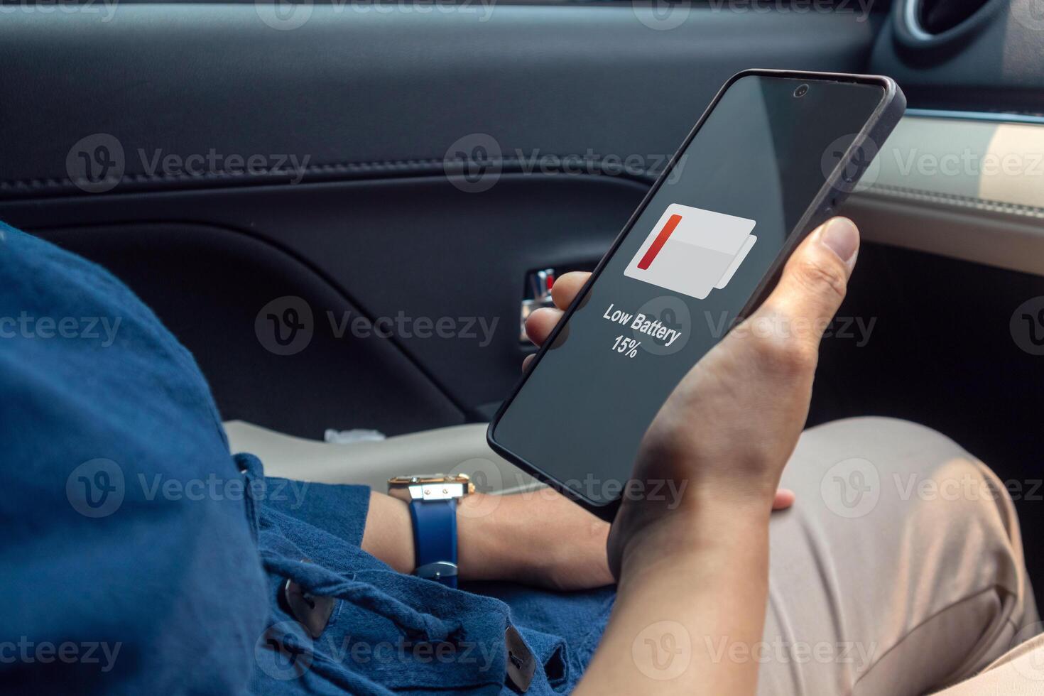Woman in car holding a mobile phone with low battery symbol on screen. Running out of battery while on the go. photo