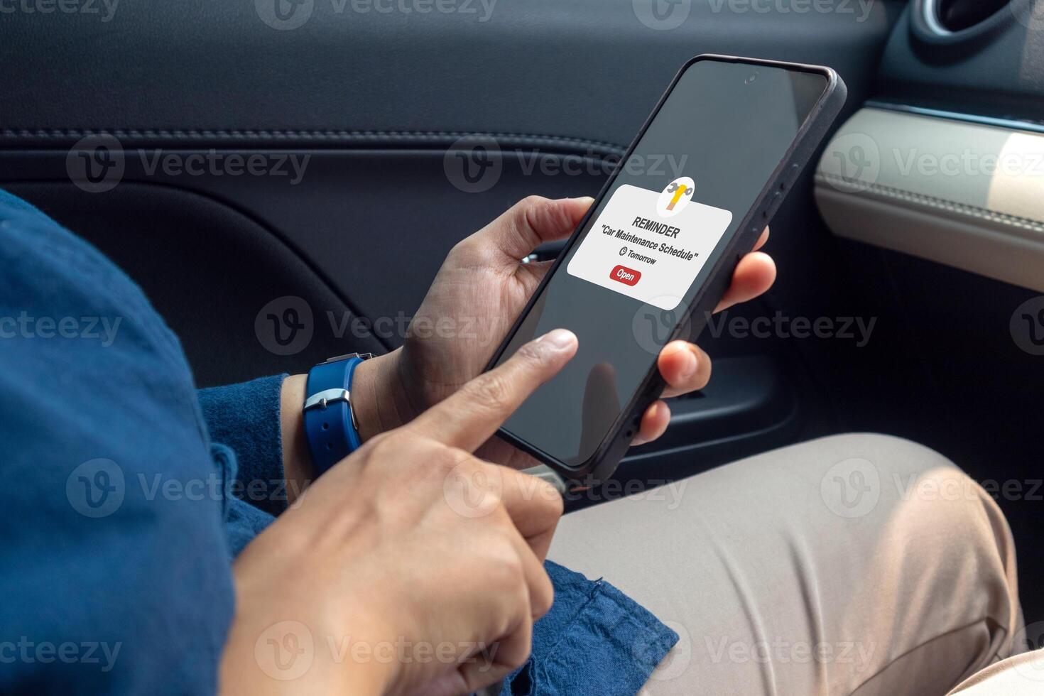 Woman in car holding a mobile phone with car maintenance schedule reminder notification on screen photo