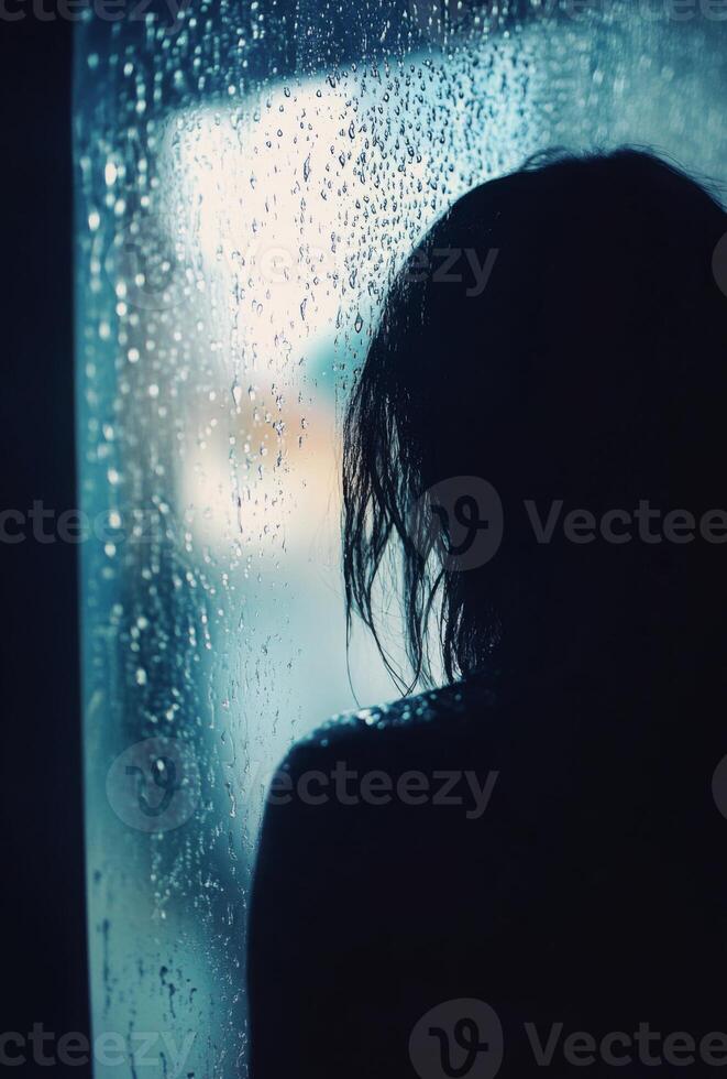 A person staring out of a rain-soaked window, with raindrops running down the glass, lost in contemplation photo