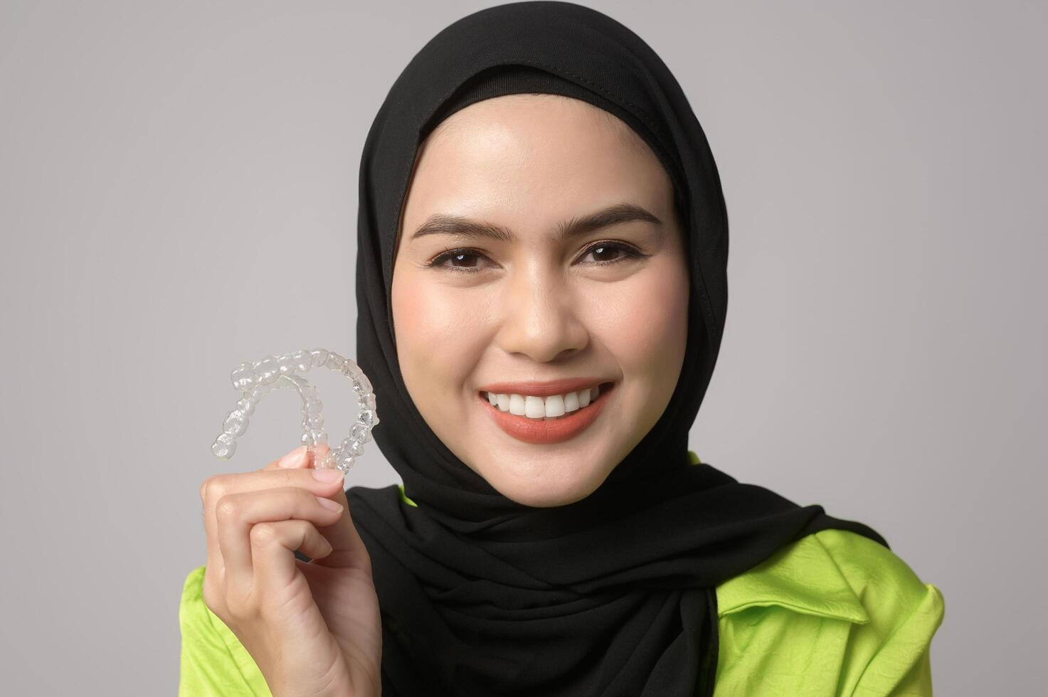 Muslim woman with hijab holding invisalign braces in studio photo