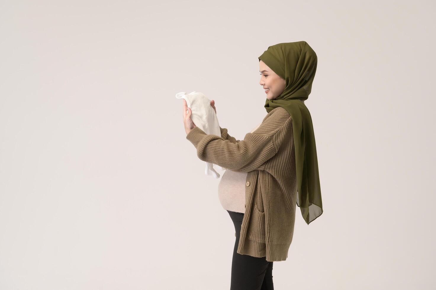 Portrait of Pregnant muslim woman in hijab holding baby cloth over white background studio photo