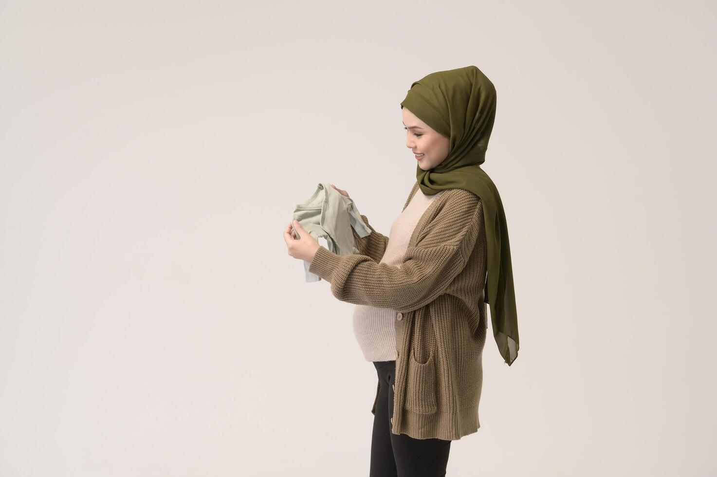 Portrait of Pregnant muslim woman in hijab holding baby cloth over white background studio photo