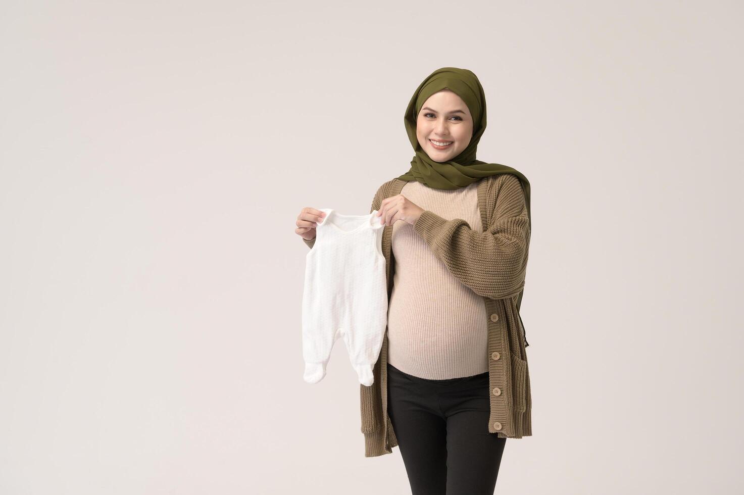 Portrait of Pregnant muslim woman in hijab holding baby cloth over white background studio photo