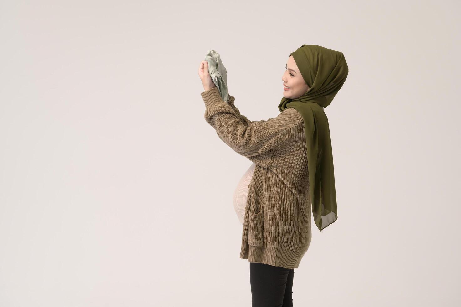 Portrait of Pregnant muslim woman in hijab holding baby cloth over white background studio photo