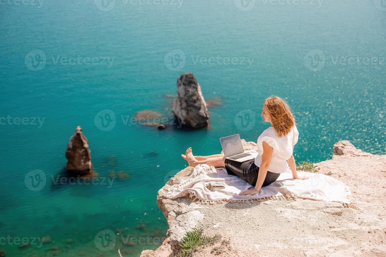 Freelance women sea working on the computer. Good looking middle aged woman typing on a laptop keyboard outdoors with a beautiful sea view. The concept of remote work. photo