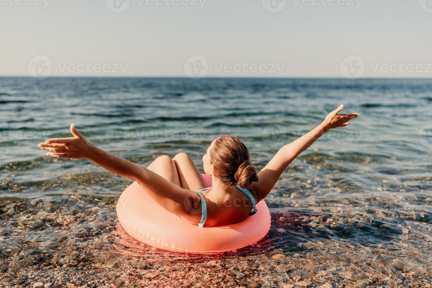 A woman is floating on a pink inflatable raft in the ocean. She is smiling and she is enjoying herself. photo