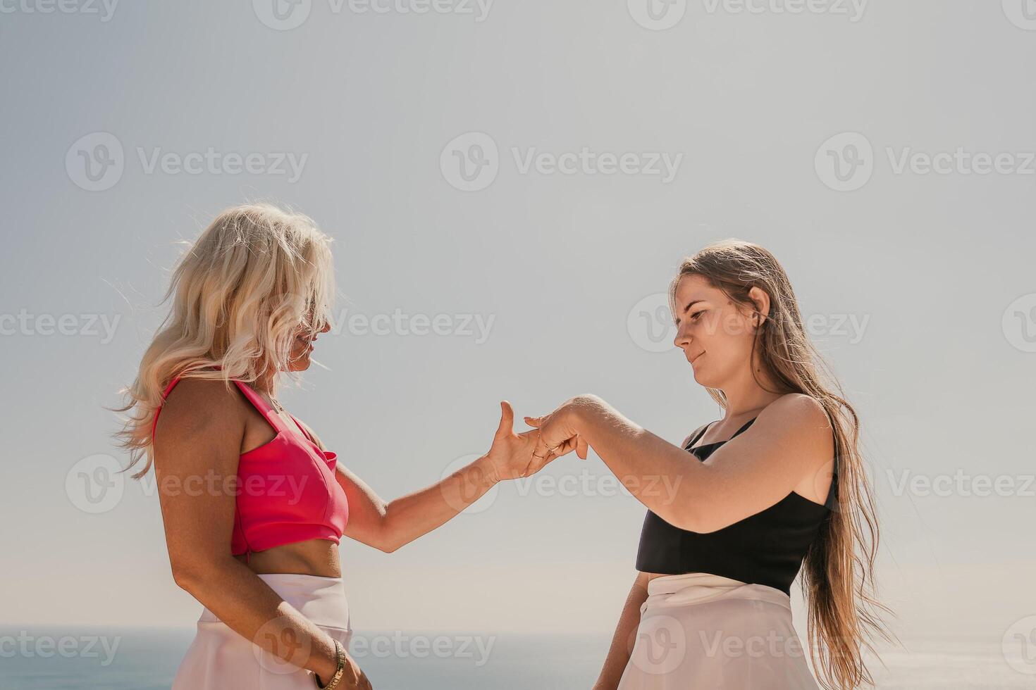 Two women are standing on a beach, one wearing a black tank top and the other wearing a pink top. They are both smiling and seem to be enjoying their time together. photo