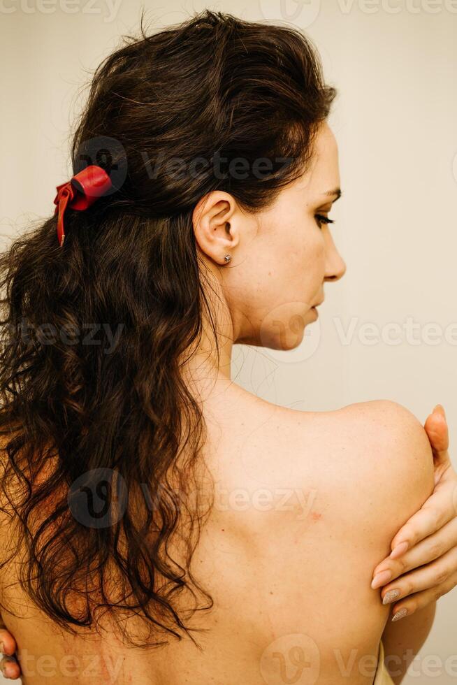 A woman with long hair is wearing a red ribbon in her hair. She is looking at something in the mirror. photo
