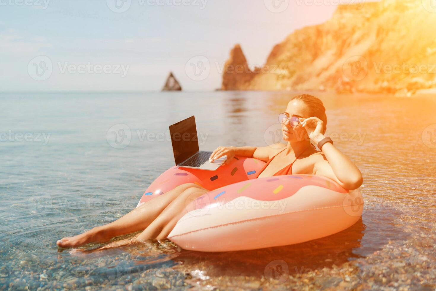 Woman laptop sea. Freelancer woman in sunglases floating on an inflatable big pink donut with a laptop in the sea. People summer vacation rest lifestyle concept photo