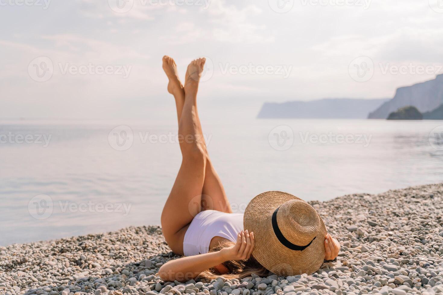 A woman is laying on the beach wearing a straw hat and a white bikini. She is enjoying the sun and the beach. photo