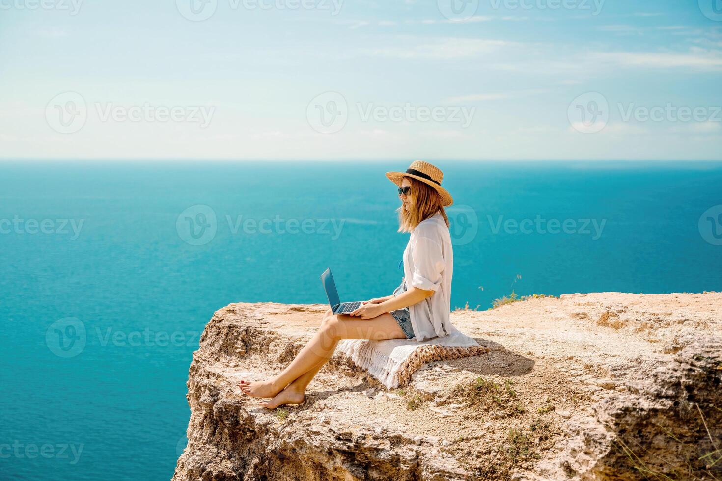 Freelance woman working on a laptop by the sea, typing away on the keyboard while enjoying the beautiful view, highlighting the idea of remote work. photo