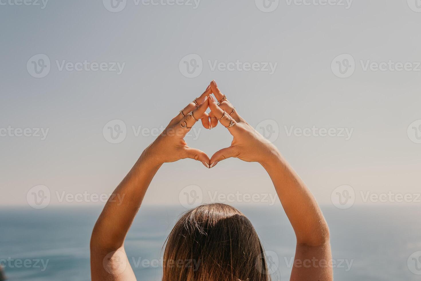 A woman is holding her hands together in a heart shape, with her arms extended towards the ocean. Concept of peace and relaxation, as the woman is enjoying the beauty of the ocean. photo