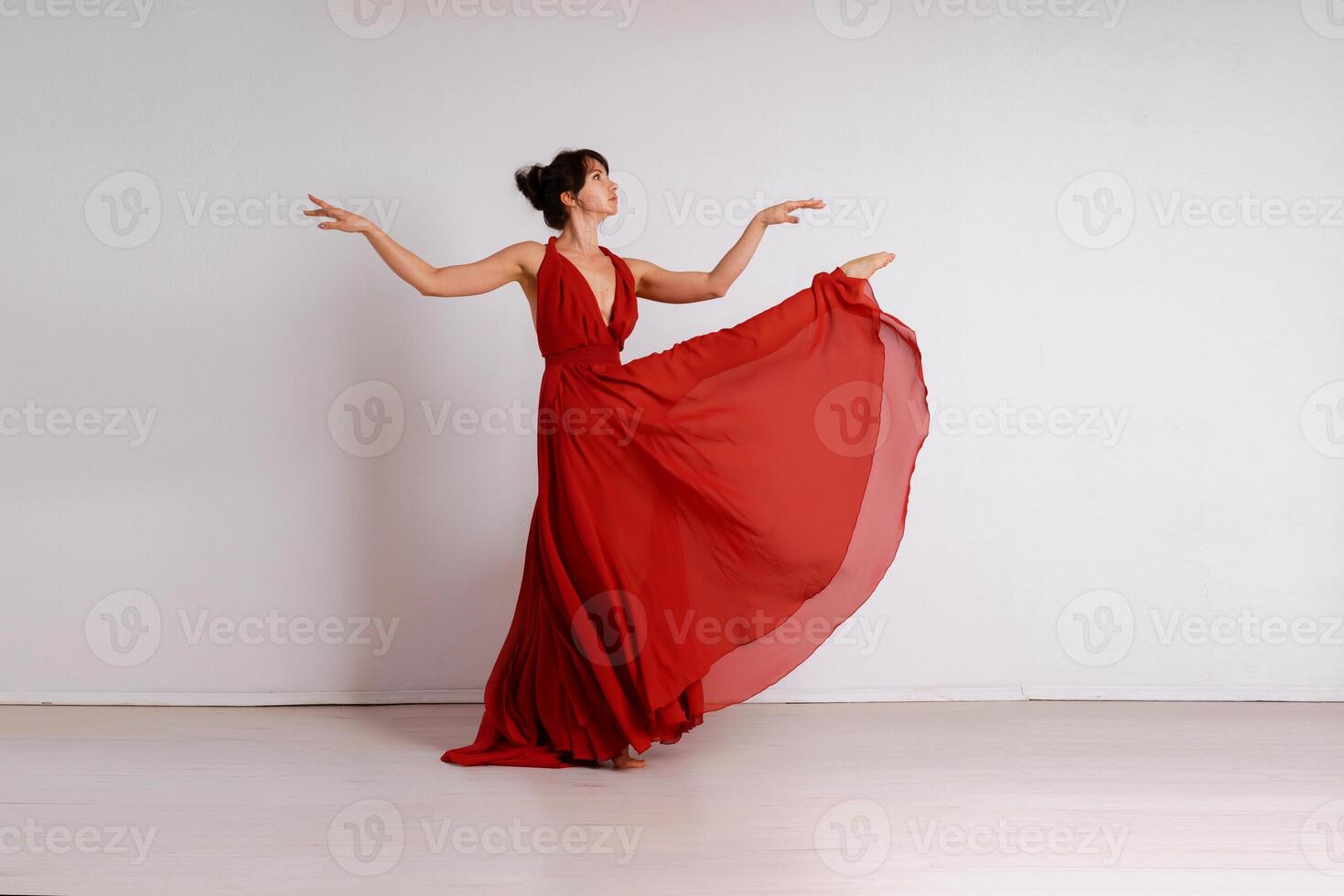 Dancer in a red flying dress. Woman ballerina dancing on a white studio background photo