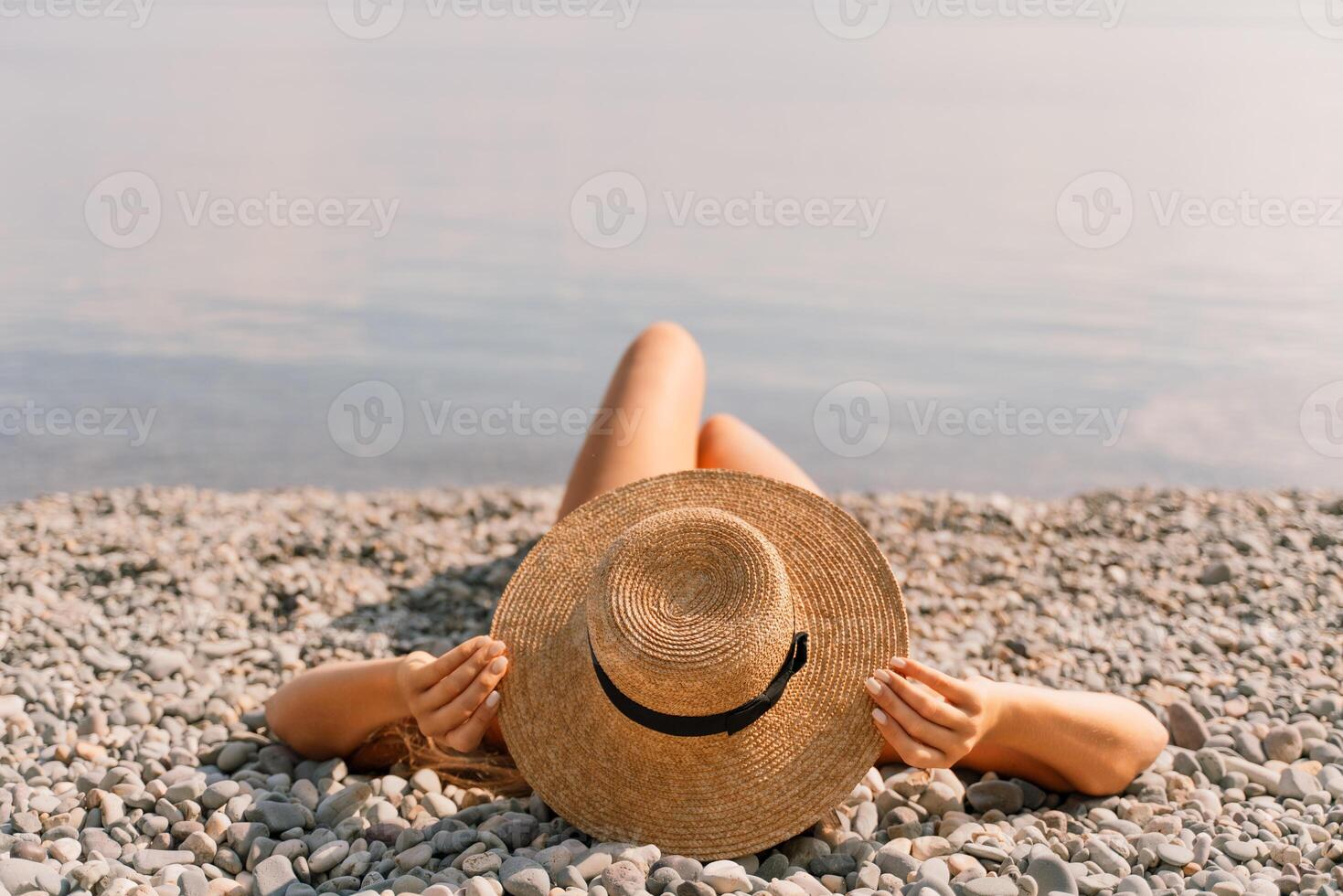 A woman is laying on the beach wearing a straw hat. She is relaxed and enjoying the sun. photo