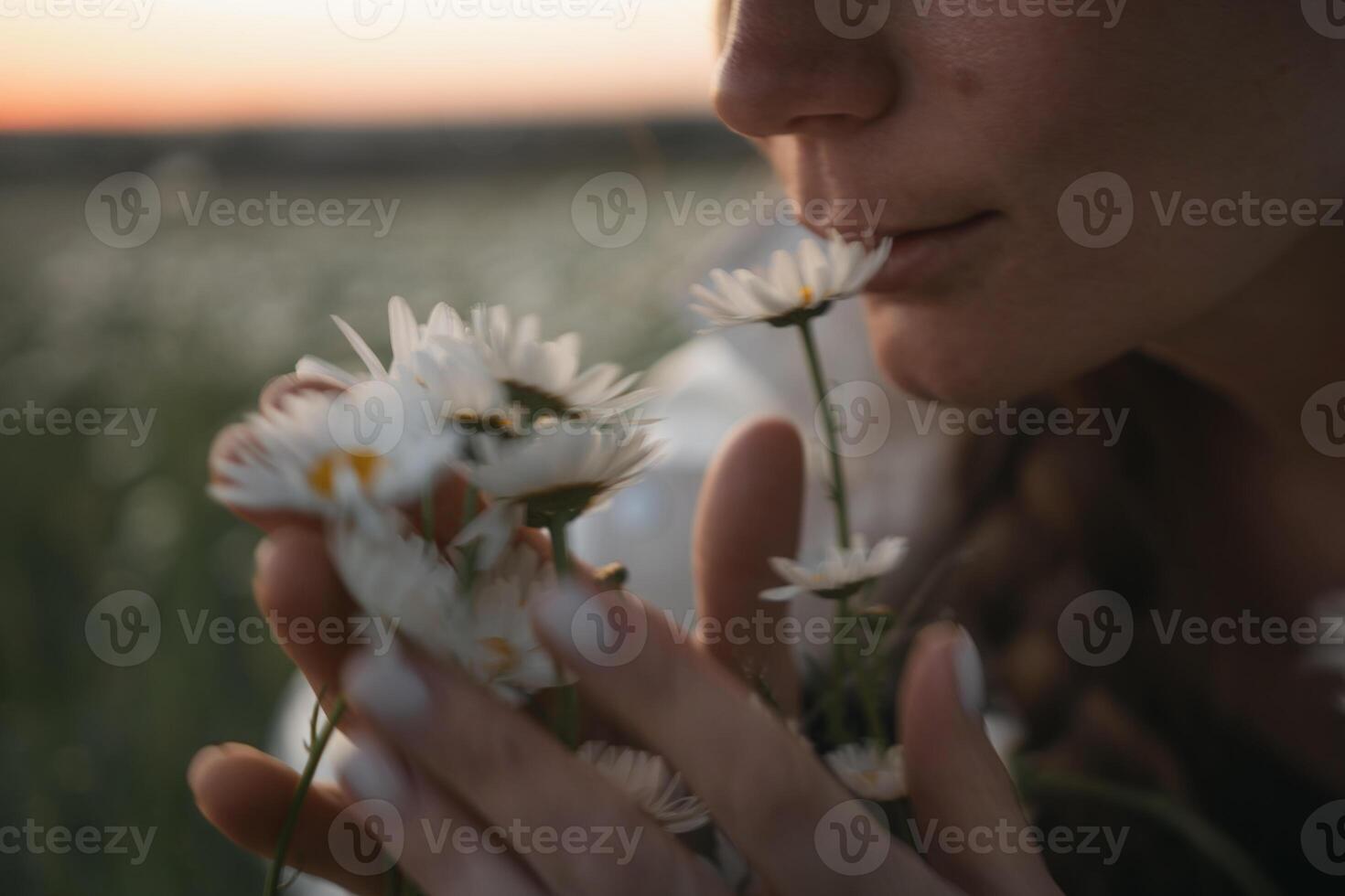 A woman is smelling a bunch of white flowers. The flowers are in a field and the woman is standing in the grass. photo