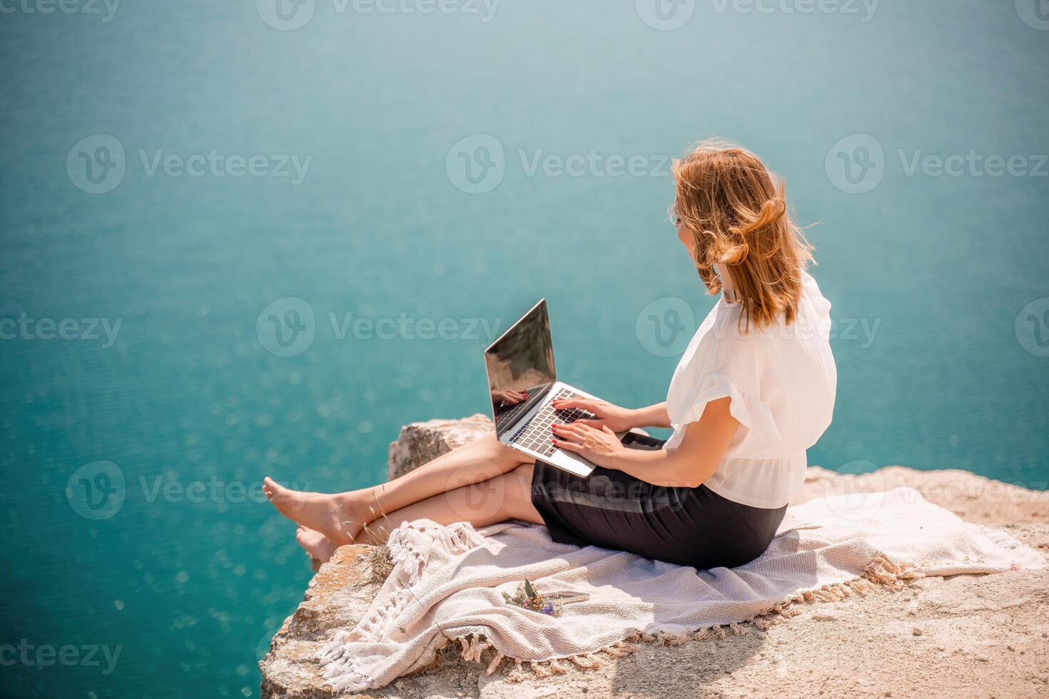 Freelance woman working on a laptop by the sea, typing away on the keyboard while enjoying the beautiful view, highlighting the idea of remote work. photo