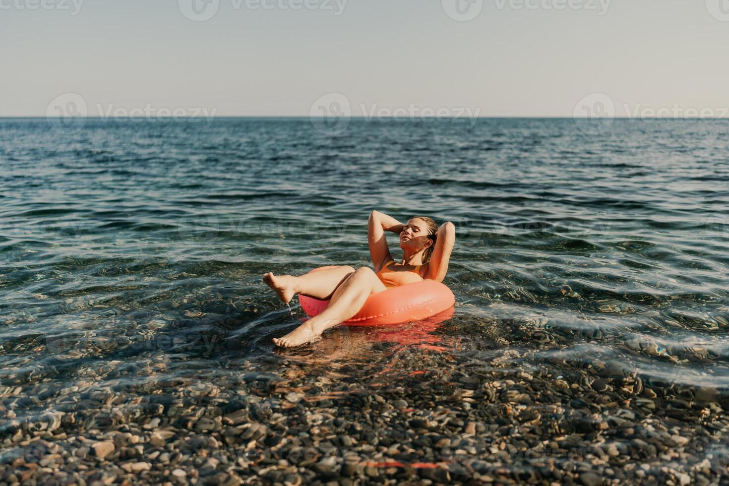 A woman is floating on a red inflatable tube in the ocean photo