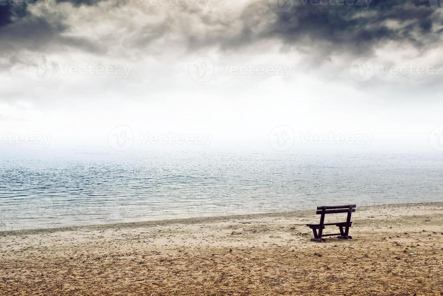 Empty wooden bench on the beach in cloudy weather photo