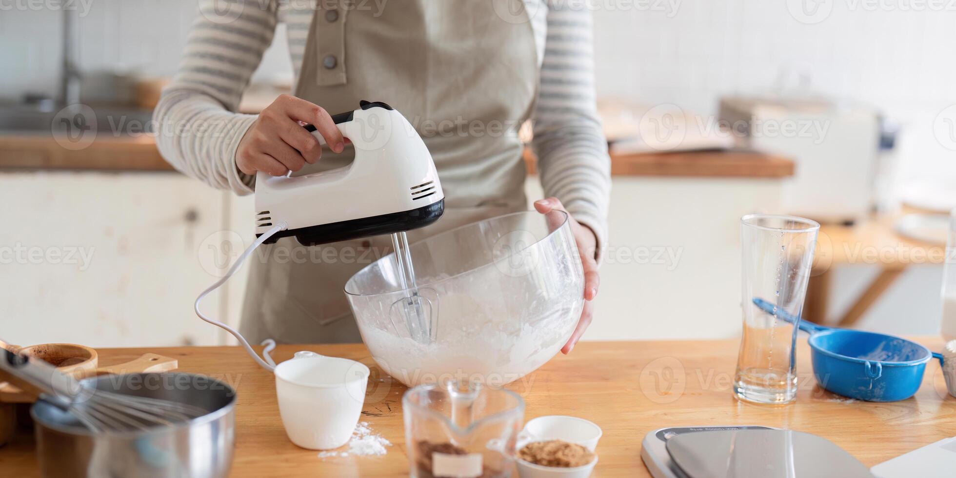 Woman using hand mixer to prepare dessert batter photo