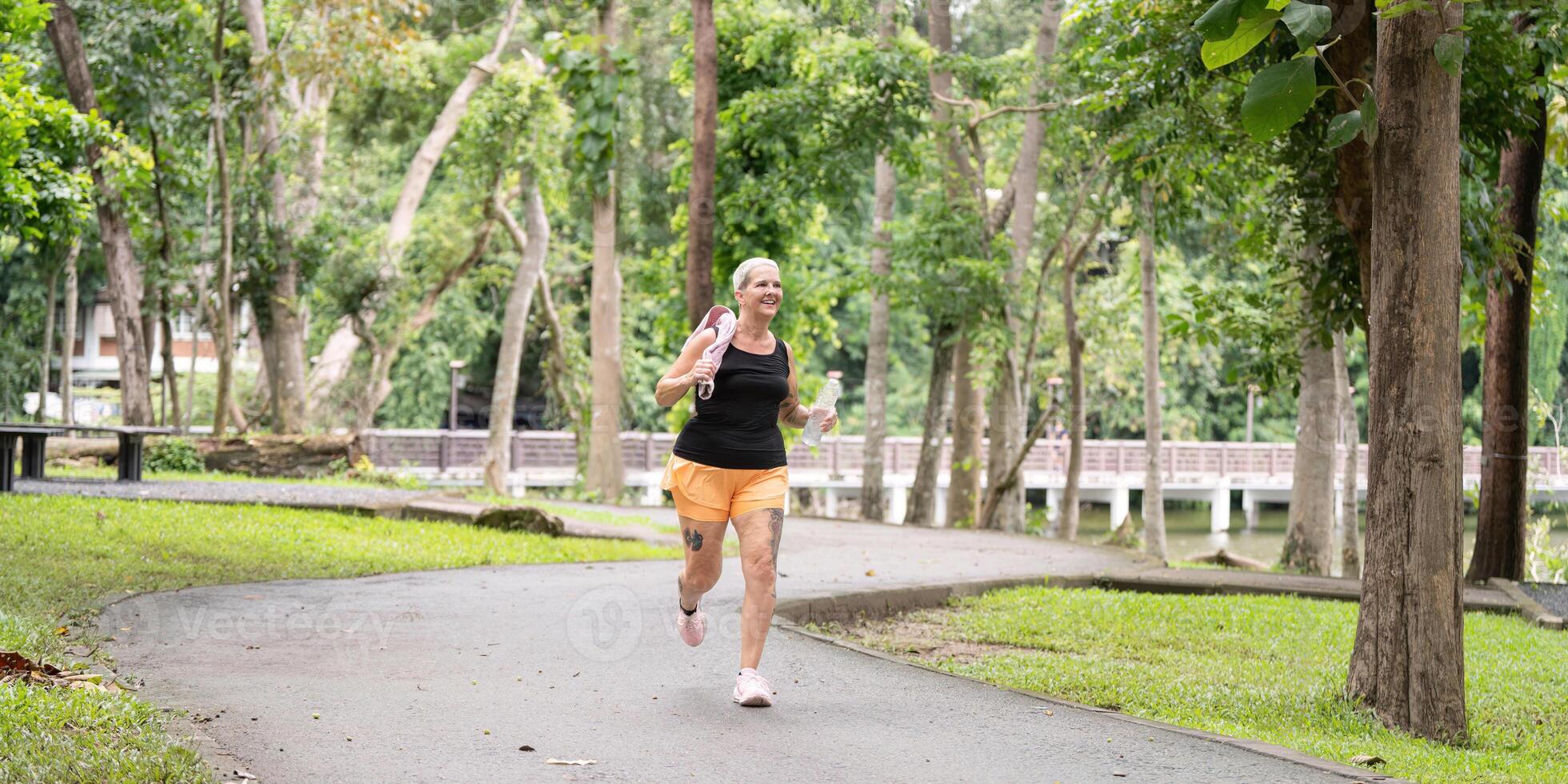 Senior woman jogging through scenic park trail photo