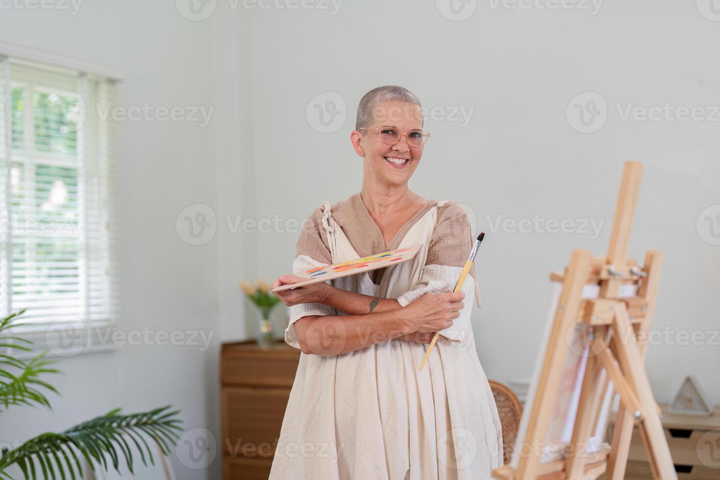 Smiling senior woman holding color palette by easel in studio photo