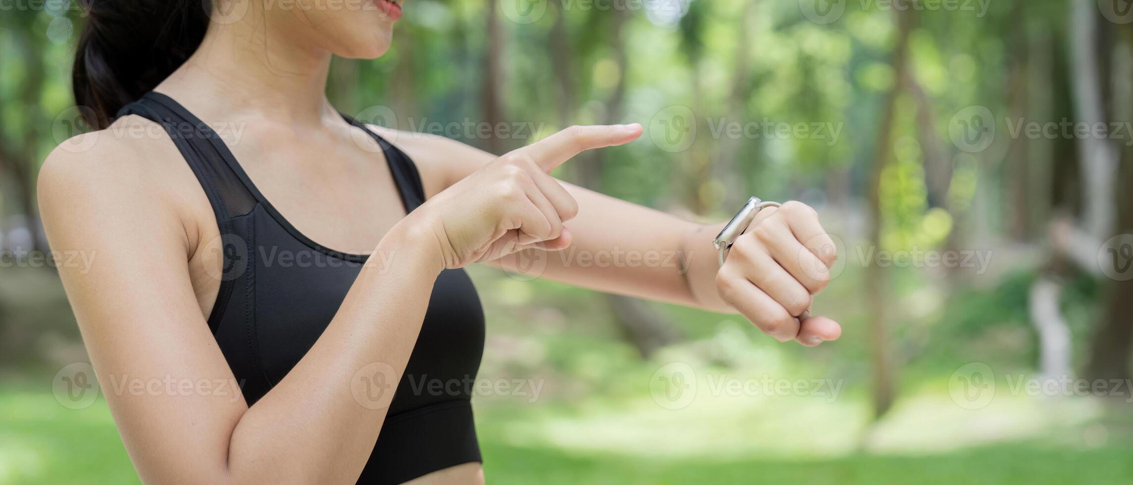 Asian young adult woman interacting with smartwatch in green park photo