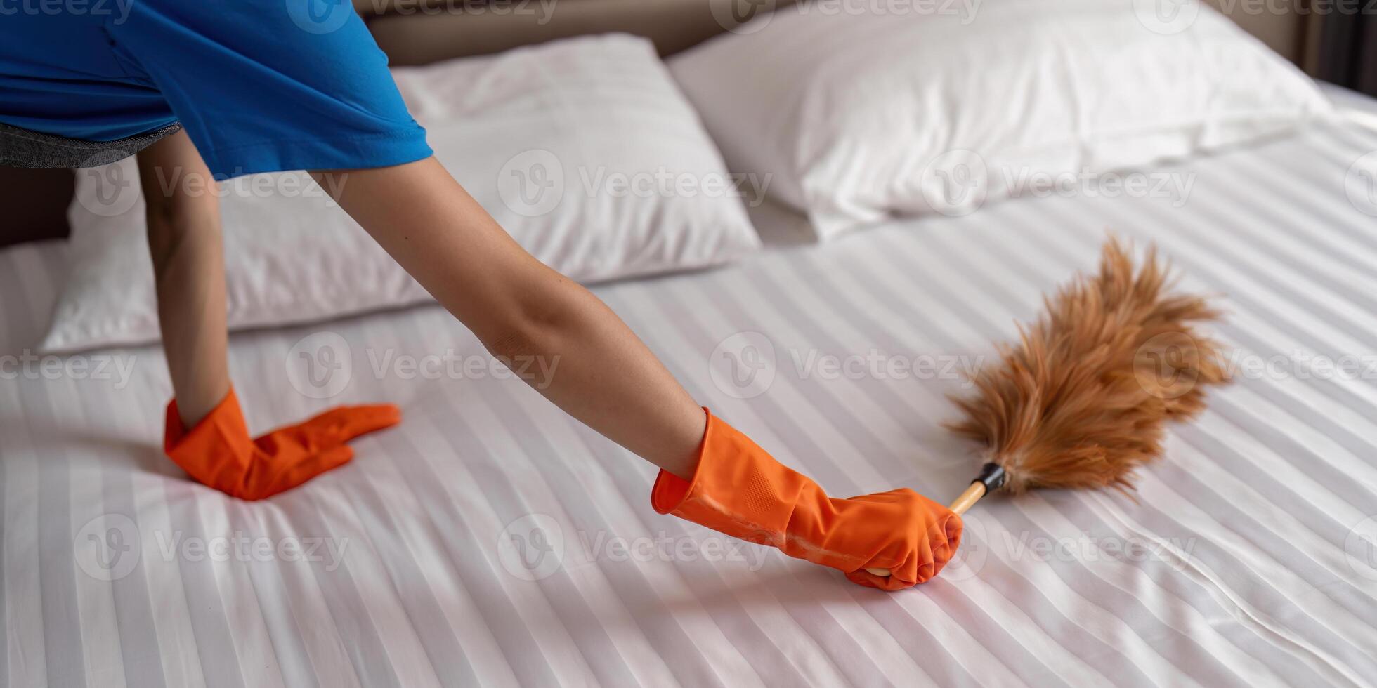 Housekeeper cleaning bed with orange gloves and duster photo