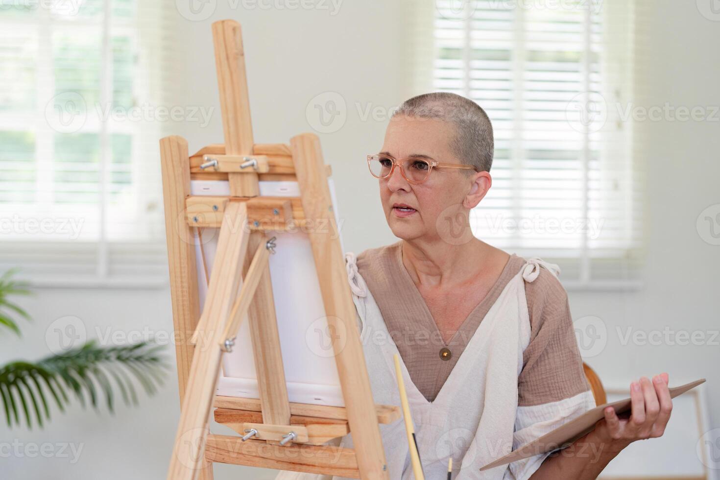 Senior woman observing her progress while painting at easel photo