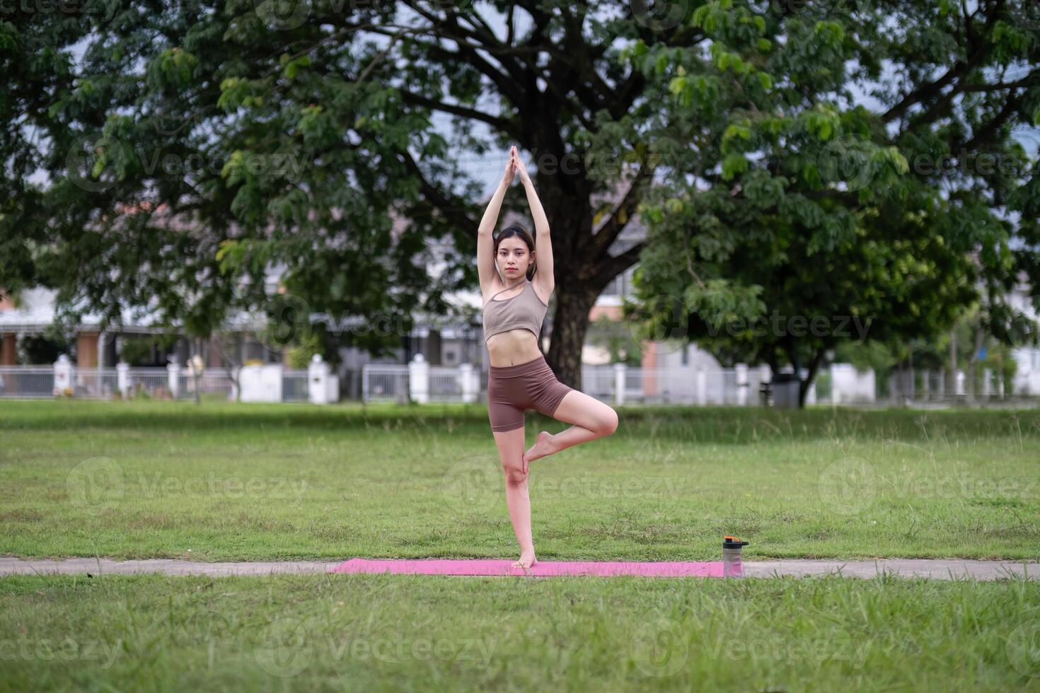 Young Woman Balancing in Tree Pose on Yoga Mat Outdoors photo