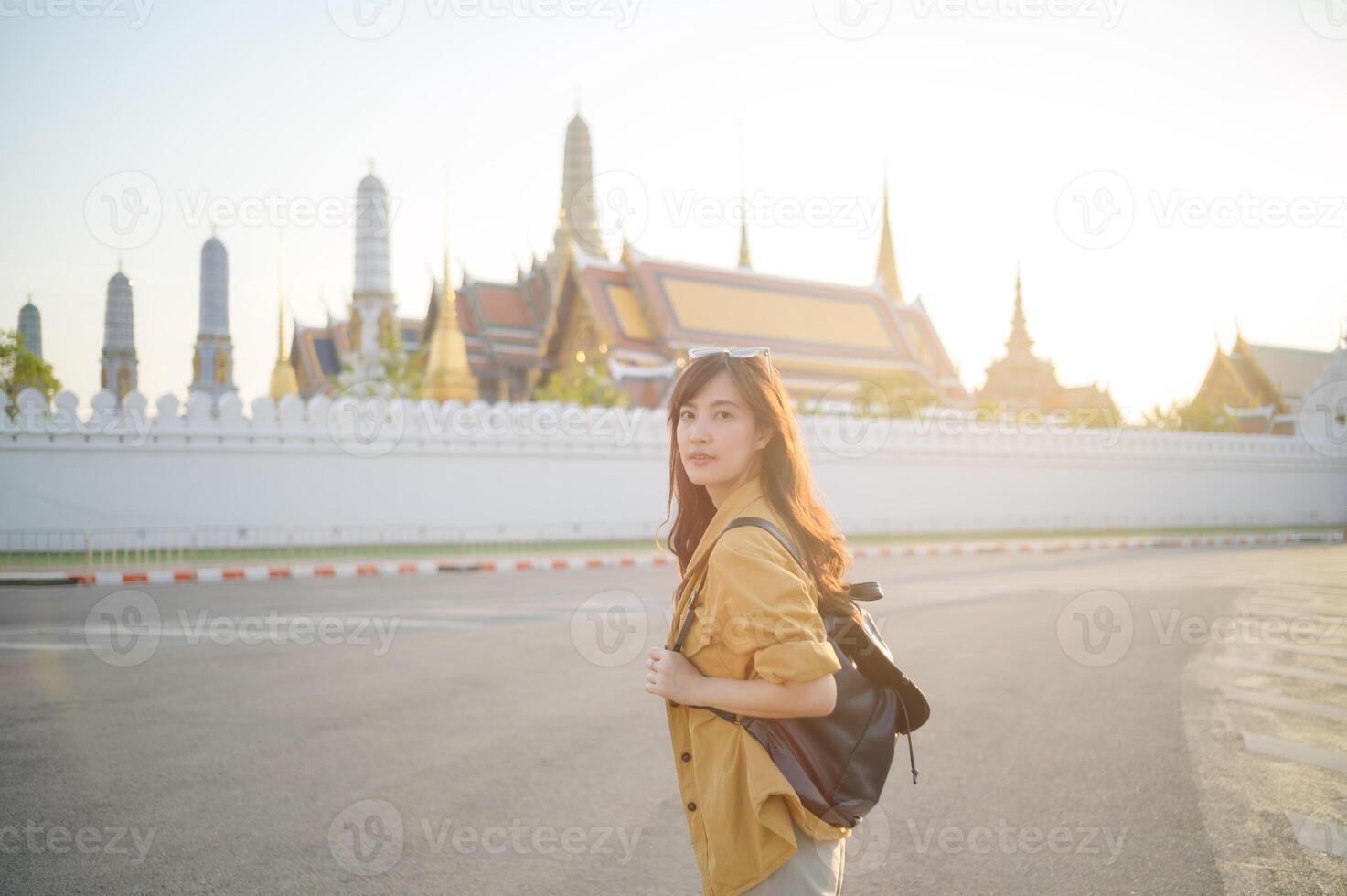 Traveler asian woman in her 30s, backpack slung over her shoulder, explores the intricate details of Wat Pra Kaew with childlike wonder. Sunlight dances on the golden rooftops. photo