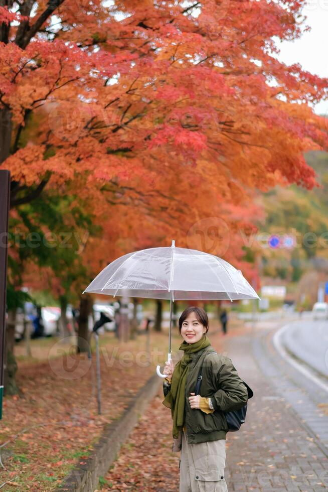 Asian woman with an umbrella embraces the joy of fall amid the rain. A cheerful and happy portrait capturing the beauty of nature's colors. photo