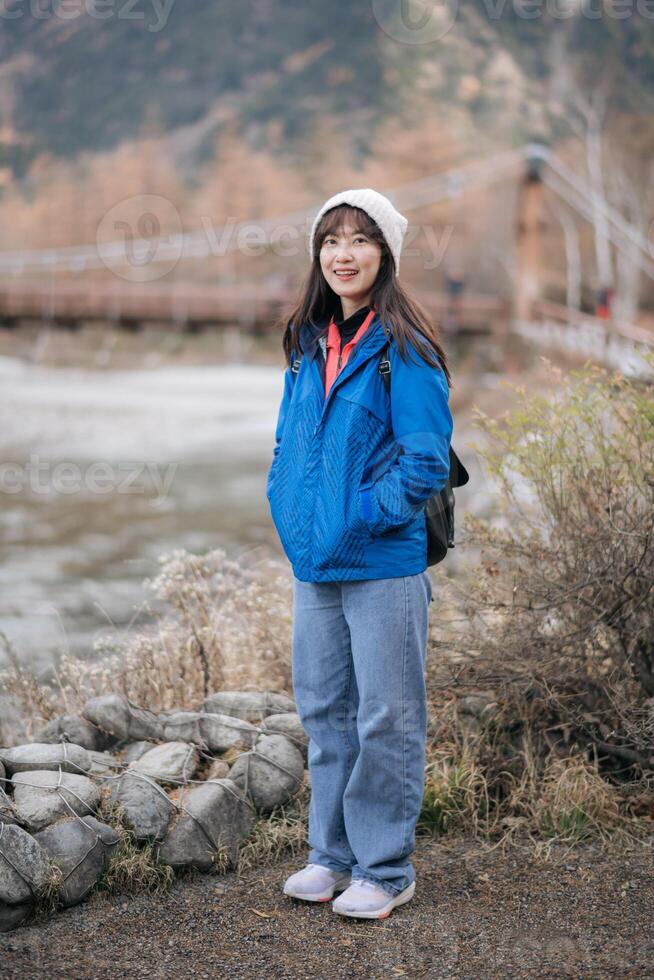 Excitement in nature, Asian woman in a blue jacket enjoys the orange hues of fall. A stylish traveler in Japan, standing alone, reflecting on the journey's joy. photo