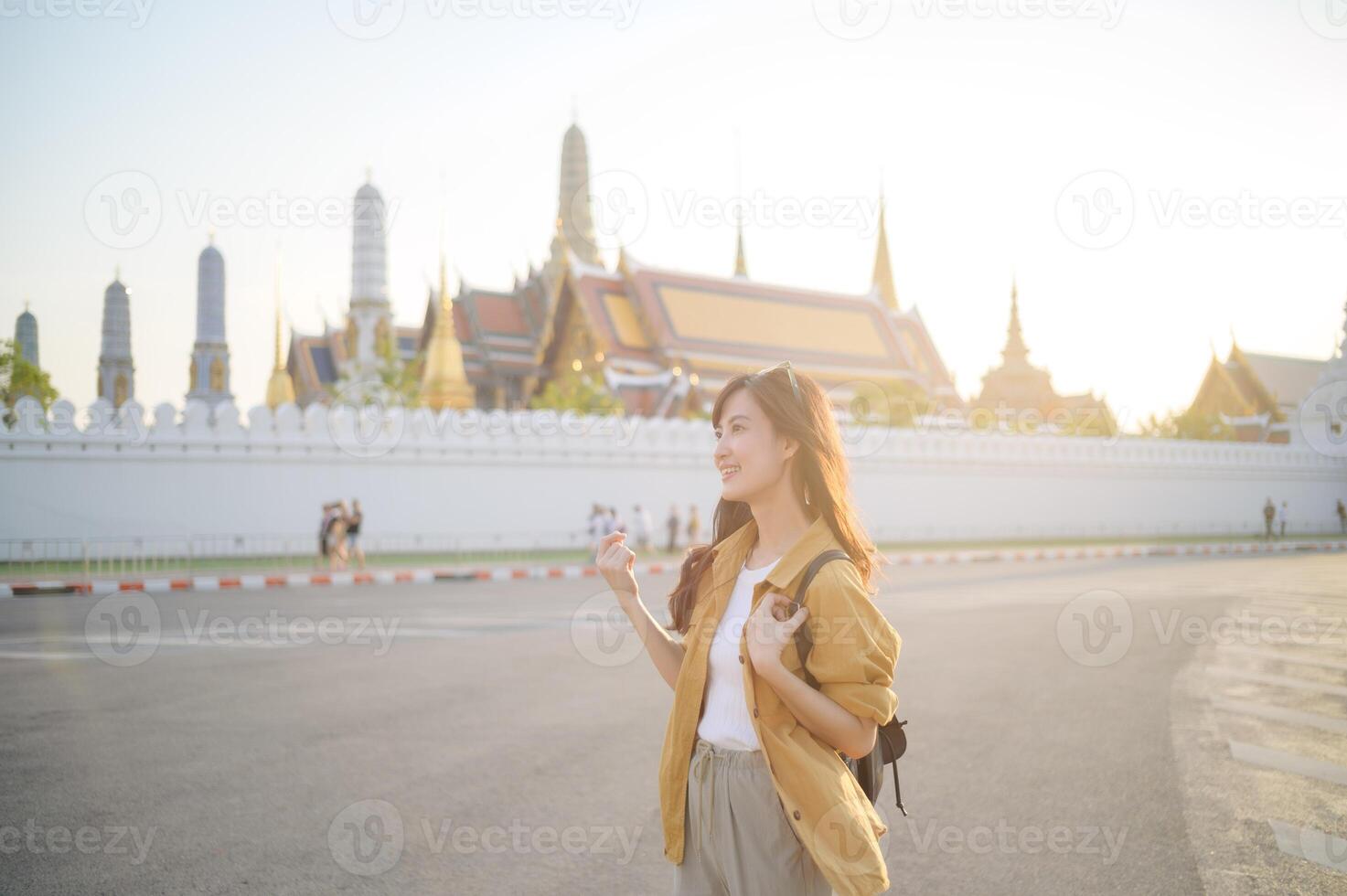 Traveler asian woman in her 30s, backpack slung over her shoulder, explores the intricate details of Wat Pra Kaew with childlike wonder. Sunlight dances on the golden rooftops. photo