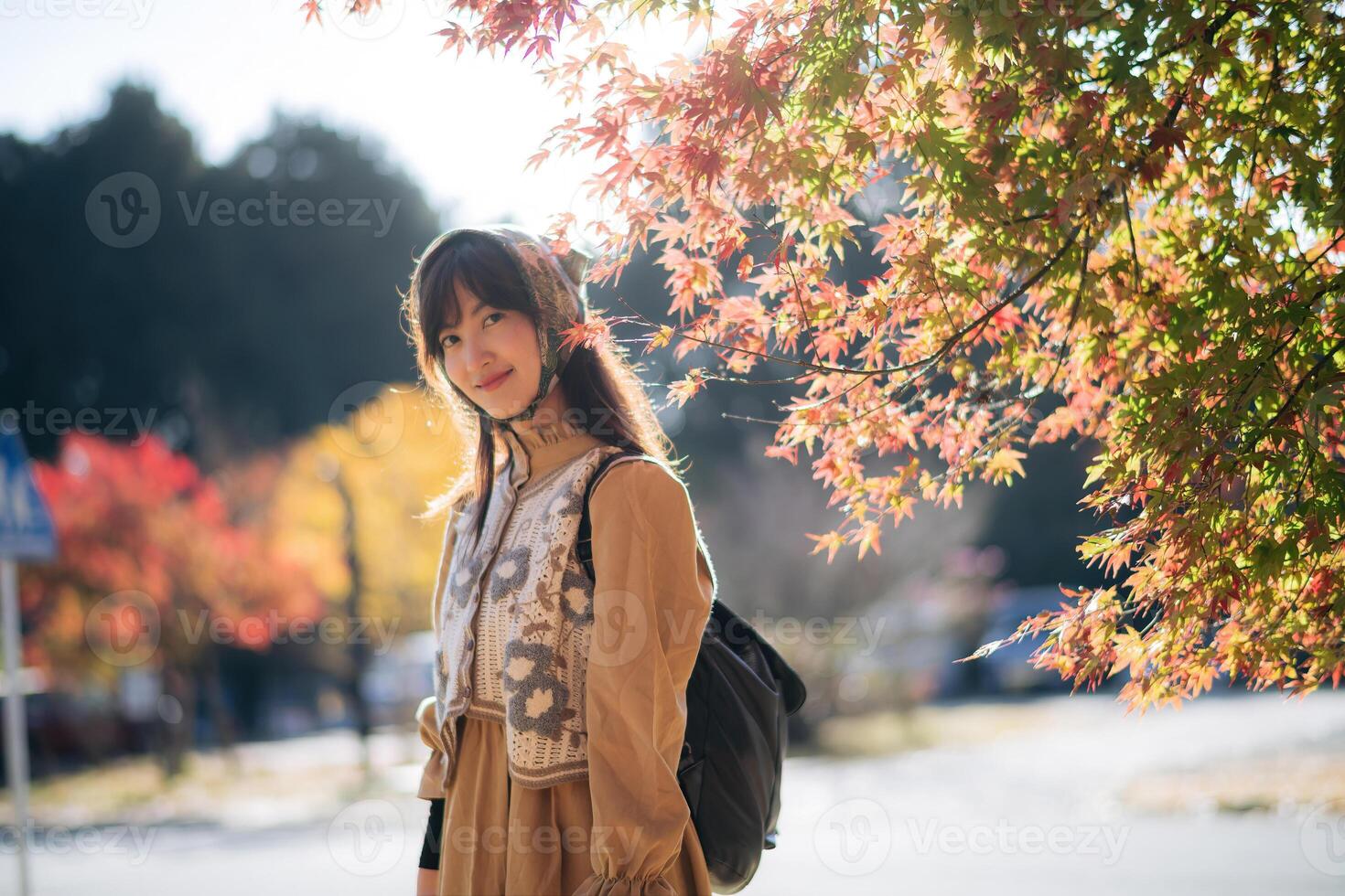Asian woman in Kyoto's fall, wearing a casual dress, enjoys nature's beauty, capturing cheerful smiles amid vibrant foliage and the scenic charm of Japan. photo